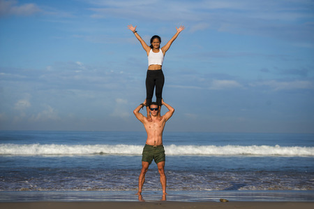 young attractive and concentrated couple of acrobats practicing acro yoga balance and meditation exercise on beautiful beach under a blue sky in mind and body control and healthy lifestyleの写真素材