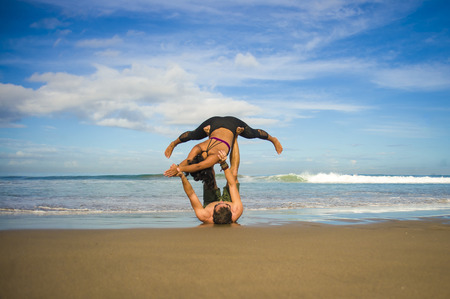 outdoors lifestyle portrait young attractive and concentrated couple of yoga acrobats practicing acroyoga balance and meditation exercise on beautiful beach in mind and body teamwork controlの写真素材