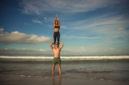 outdoors lifestyle portrait young attractive and concentrated couple of yoga acrobats practicing acroyoga balance and meditation exercise on beautiful beach in mind and body teamwork controlの写真素材