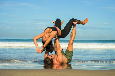 young attractive and concentrated couple of acrobats practicing acro yoga balance and meditation exercise on beautiful beach under a blue sky in mind and body control and healthy lifestyleの写真素材