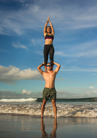 young attractive and concentrated couple of acrobats practicing acro yoga balance and meditation exercise on beautiful beach under a blue sky in mind and body control and healthy lifestyleの写真素材