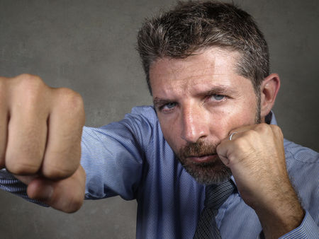 head and shoulders dramatic portrait of middle aged upset and fierce businessman boxing throwing...