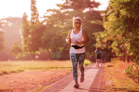 middle aged 40s or 50s happy and attractive woman with grey hair training at city park with green...
