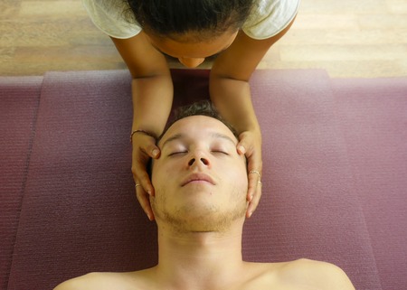 young beautiful and exotic Asian Balinese therapist woman giving traditional head and facial Thai massage to Caucasian man in harmony health care and wellness lifestyle at relaxing wellness spaの写真素材