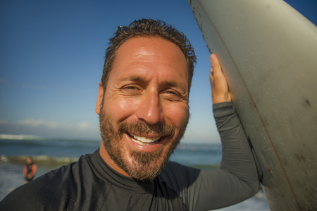 lifestyle beach closeup portrait of handsome and attractive surfer man in neoprene swimsuit holding surf board posing cool after surfing enjoying Summer water sport and holidaysの写真素材