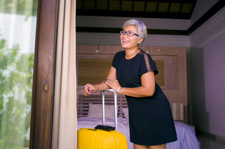 lifestyle portrait of natural attractive and happy middle aged Asian woman in stylish Summer dress arriving to hotel opening room balcony door looking delighted enjoying travel holidays getawayの写真素材