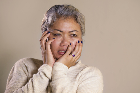 dramatic portrait of attractive sad and depressed middle aged Asian woman crying helpless suffering depression problem and anxiety crisis in pain and desperate face expression isolated on greyの写真素材
