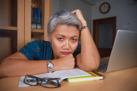 office lifestyle portrait of depressed and overworked middle aged attractive Asian woman working in stress on laptop computer desk feeling upset and overwhelmed in upset face expressionの写真素材