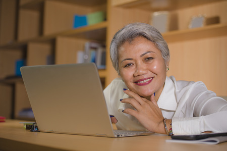 lifestyle office portrait of attractive and happy successful middle aged Asian woman working at laptop computer desk smiling confident in entrepreneur business and financial successの写真素材