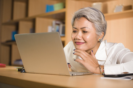 natural lifestyle office portrait of attractive and happy successful mature Asian woman working at...