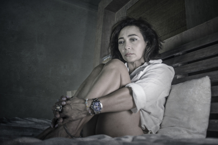 dramatic lifestyle portrait of attractive sad and depressed middle aged around 50s woman feeling upset alone on bed suffering depression and anxiety crisis as mature lady lost and confusedの写真素材