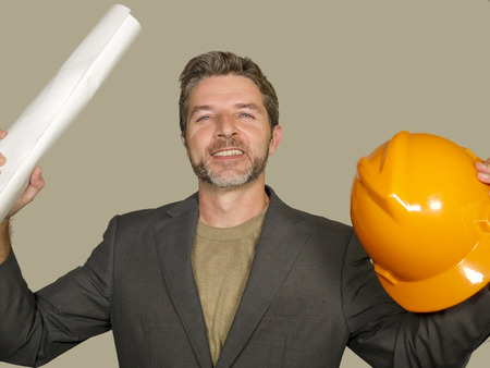 corporate portrait of young attractive and successful industrial engineer or architect holding building project blueprint and safety builder helmet happy and satisfied isolated on white backgroundの写真素材