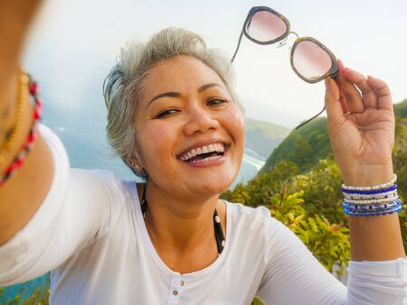 middle age 50s happy and cheerful Asian woman with grey hair taking selfie with mobile phone at...