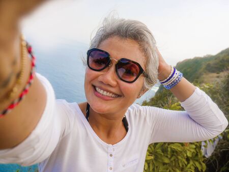 middle age 50s happy and cheerful Asian woman with grey hair taking selfie with mobile phone at...