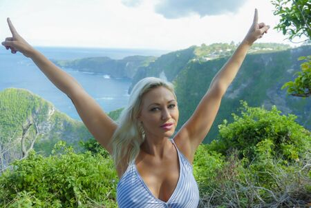 young happy and beautiful blond woman relaxed at tropical beach cliff landscape enjoying Summer holidays getaway carefree at paradise island in tourist travel destination conceptの写真素材