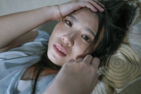 dramatic lifestyle portrait of young desperate sad and depressed Asian Korean woman sitting at home...