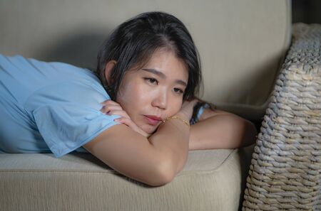 dramatic lifestyle portrait of young beautiful sad and depressed Asian Japanese woman at home sofa couch feeling overwhelmed suffering anxiety crisis and depression problem cryingの写真素材