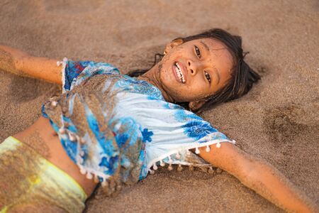 beach lifestyle portrait of young beautiful and happy Asian American mixed ethnicity child girl 7 or 8 years old playing lying on the sand having fun enjoying Summer holidaysの写真素材