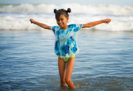 holiday beach lifestyle portrait of young beautiful and happy Asian child girl 8 or 9 years old with cute double buns hair style playing carefree in the sea enjoying Summer vacation having fun aloneの写真素材