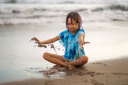 beach lifestyle portrait of young beautiful and happy Asian American mixed ethnicity child girl 7 or 8 years old playing with sand having fun enjoying Summer holidays isolated on sea backgroundの写真素材