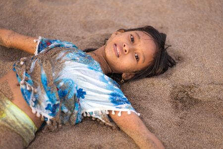 beach lifestyle portrait of young beautiful and happy Asian American mixed ethnicity child girl 7 or 8 years old playing lying on the sand having fun enjoying Summer holidaysの写真素材
