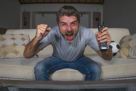 30s or 40s football fan man watching soccer game celebrating his team scoring goal crazy happy screaming cheering his team sitting at home living room couch gesturing in spastic celebrationの写真素材