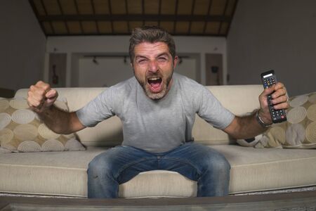 30s or 40s football fan man watching soccer game celebrating his team scoring goal crazy happy screaming cheering his team sitting at home living room couch gesturing in spastic celebrationの写真素材