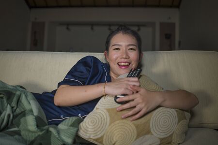 young beautiful happy and cheerful Asian Korean woman watching television comedy movie or hilarious...