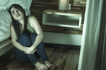 dramatic lifestyle portrait of young depressed and sad Asian Korean woman sitting on floor at bedroom next to bed suffering depression problem and anxiety crisis feeling desperate and lonelyの写真素材