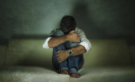 dramatic portrait of young attractive depressed and sad shady man at home couch crying lost in pain...