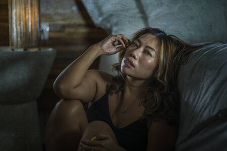 dramatic home lifestyle portrait of young beautiful sad and depressed Asian Indonesian woman in...