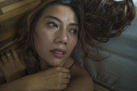 dramatic home lifestyle portrait of young beautiful sad and depressed Asian Indonesian woman in...