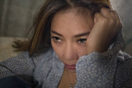 dramatic lifestyle portrait of young beautiful sad and depressed woman thoughtful and confused at home couch feeling broken heart suffering depression crisis and anxiety problemの写真素材