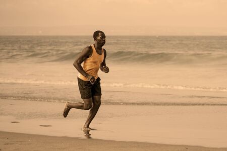 athletic full body portrait of young attractive and fit black afro American man running on the beach...