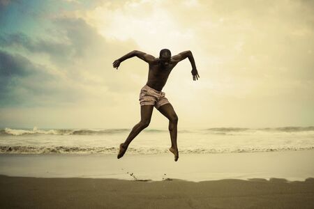 dramatic contemporary dance choreographer doing ballet beach workout . young attractive and athletic afro black American man dancing on sunrise jumping doing performance rehearsalの写真素材
