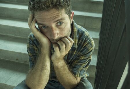 dramatic lifestyle portrait of young depressed and sad man sitting alone outdoors on dark street...