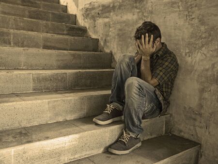 dramatic lifestyle portrait of young depressed and sad man sitting alone outdoors on dark street...