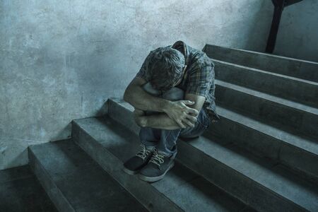 dramatic portrait of young depressed and desperate man sitting outdoors on dark grunge street corner staircase feeling sick suffering depression problem and anxiety crisis in mental health conceptの写真素材