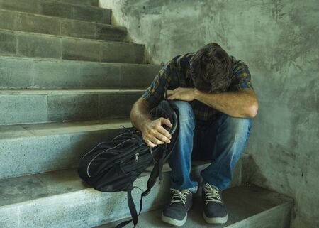 anti sexual discrimination and against homophobia campaign. Young sad and depressed college student man sitting on staircase desperate victim of harassment suffering bullying and abuseの写真素材