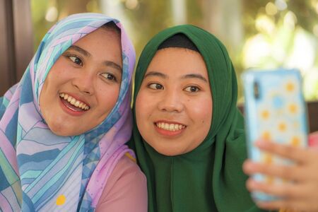 Muslim teenager student girlfriends selfie. Happy and pretty Asian Indonesian girls in traditional...