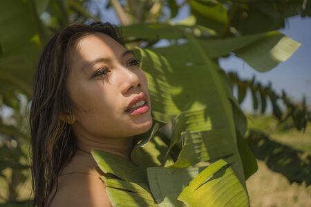 young beautiful and happy Asian Indonesian woman in bikini posing between leaves of banana tree smiling natural isolated on exotic tropical background in Summer holiday travel and beauty conceptの写真素材