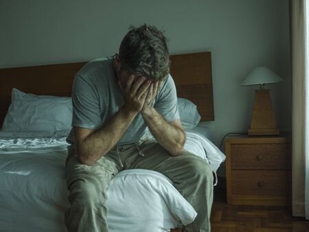 Attractive depressed and upset man at home bedroom . dramatic lifestyle portrait of 30s to 40s handsome guy sitting sad on bed feeling worried and desperate suffering depression problemの写真素材