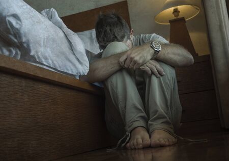 dramatic home portrait of young depressed and desperate man sitting on bedroom floor next to bed suffering depression and anxiety feeling overwhelmed and helplessの写真素材