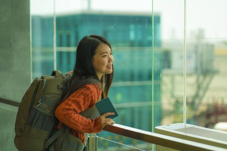 young happy and excited Asian Japanese student woman with backpack at airport departure lounge watching aircraft through glass window smiling ready for boarding in holidays travelの写真素材
