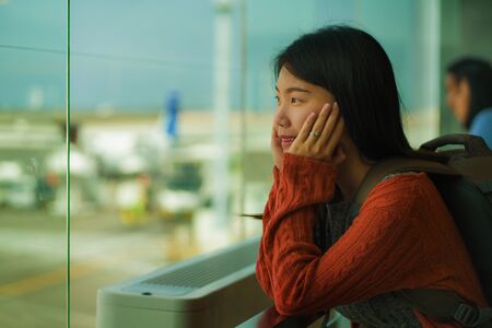 young happy and excited Asian Japanese student woman with backpack at airport departure lounge watching aircraft through glass window smiling ready for boarding in holidays travelの写真素材