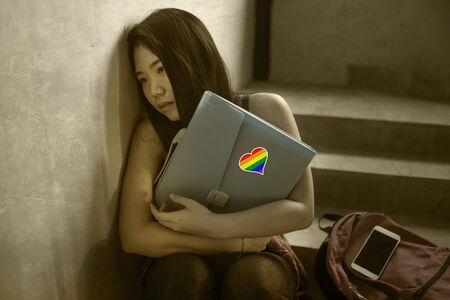 respect for homosexual and anti sexual discrimination campaign. Young beautiful depressed and scared Asian student woman with gay flag on her backpack victim of abuse and bullyingの写真素材