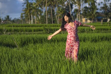 natural and fresh lifestyle portrait of  young beautiful and attractive Asian Korean woman in elegant dress walking on green rice field enjoying exotic Summer holidays trip in natureの写真素材