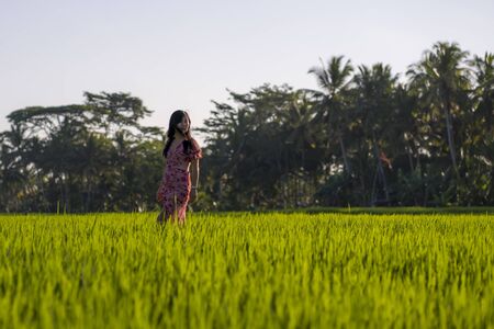 natural lifestyle portrait of young beautiful and happy Asian Chinese woman in elegant Summer dress walking carefree and relaxed at fresh tropical rice field enjoying unique travel destinationの写真素材