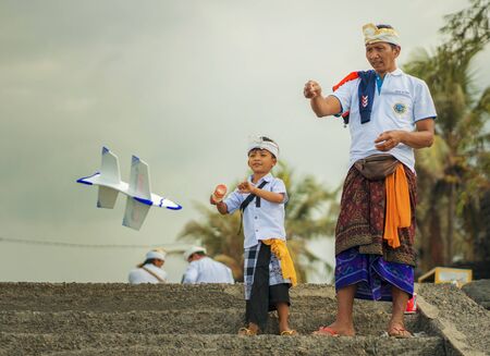 Bali / Indonesia - Sept 14th 2019 . Balinese kid and his fatherdressed in traditional custom playing with airplane polystyrene toy during a pause at Hindu sacred ceremonyのeditorial素材