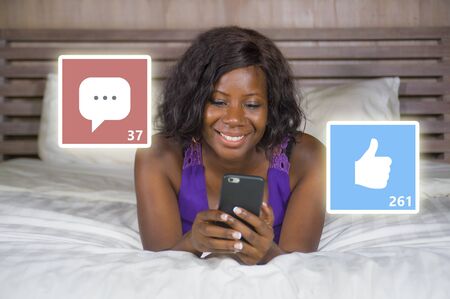 young beautiful and happy black African American woman in pajamas using mobile phone social media...